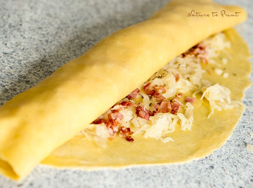 Selbstgemachte Allgäuer Krautkrapfen kurz bevor sie geschnitten werden und in die Pfanne kommen Strudelteig mit Füllung aufrollen