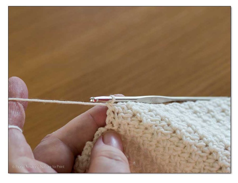 Jedes Maschenpäckchen beginnt mit einer festen Masche (FM) im Luftmaschenbogen der Vorreihe. Gehäkeltes Plaid im Wölkchenmuster: Häkeln Sie eine feste Masche (FM) in den Luftmaschenbogen der Vorreihe.