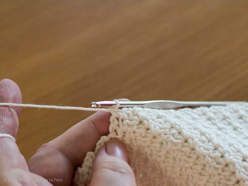 Jedes Maschenpäckchen beginnt mit einer festen Masche (FM) im Luftmaschenbogen der Vorreihe. Gehäkeltes Plaid im Wölkchenmuster: Häkeln Sie eine feste Masche (FM) in den Luftmaschenbogen der Vorreihe.